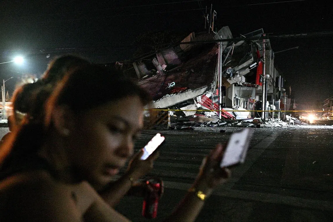 People using their phones near a collapsed building following the magnitude 7.8 quake in General Santos, southern Philippines, on June 8, 2026. 