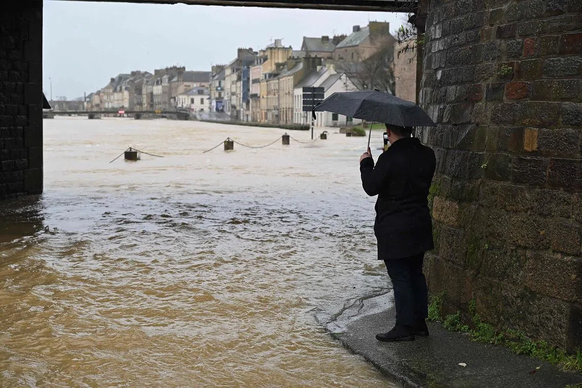 TOPSHOT - A man takes a picture of the overflowing Vilaine river in Redon, western France, on January 29, 2025. The Loire-Atlantique and Morbihan regions, as well as Ille-et-Vilaine where 600 people have been evacuated since January 26, were placed on red alert for flooding by Meteo-France on January 28, following storm Herminia. (Photo by Damien MEYER / AFP)
