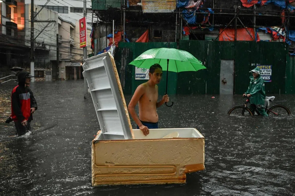 (FILES) People walk along a flooded street in Manila on July 24, 2024 amid heavy rains brought by Typhoon Gaemi. Human-induced climate change fuelled a rare string of back-to-back typhoons that battered the Philippines this year and boosted the chances of powerful storms making landfall, a new study said on December 12, 2024. (Photo by Jam Sta Rosa / AFP)