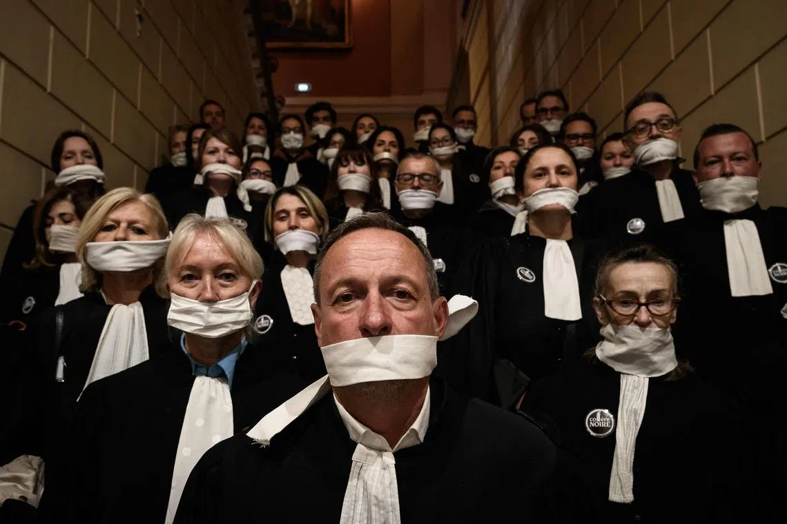 TOPSHOT - Lawyers gather with their mouths taped shut, in front of the Chambery courthouse, during a demonstration by lawyers against the "SURE" (Useful, Fast and Effective Sentencing) draft bill, in particular its proposal to introduce plea bargaining in criminal matters, as the French Senate begins debating the text, in Chambery on April 13, 2026. Lawyers across France staged a nationwide "Justice morte" (Dead Justice) stoppage called by most of the country's 164 bar associations, as the Senate opened debate on the bill which the government says is needed to tackle a backlog of more than 6,000 pending criminal cases. (Photo by JEFF PACHOUD / AFP)