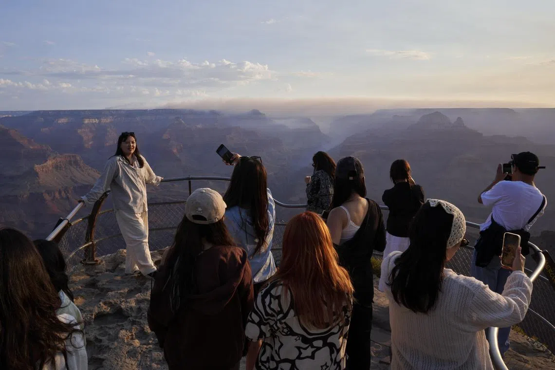 A visitor from South Korea posing for a sunrise photo at Mather Point on the South Rim in Grand Canyon Village, Arizona, as smoke rises in the distance from the Dragon Bravo Fire on the North Rim of the Grand Canyon, on July 15.