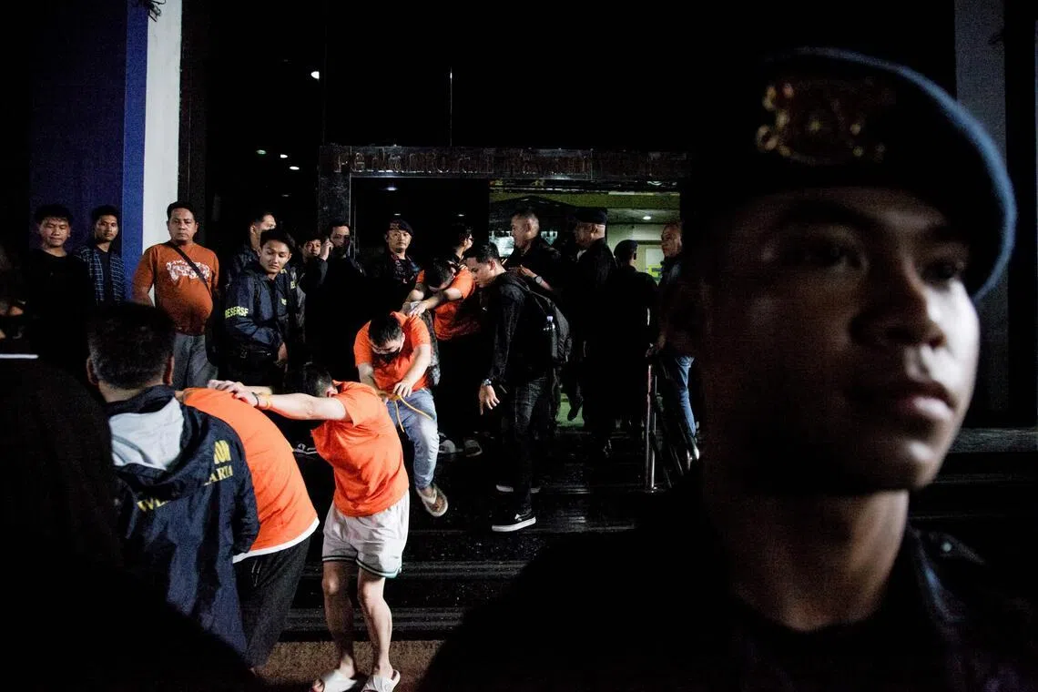 TOPSHOT - Suspected online gambling operators (in orange) walk towards buses for transfer after a police raid at the Hayam Wuruk Plaza office building in Jakarta on May 10, 2026. Indonesian police and immigration authorities said they arrested 321 foreign nationals, including suspects from Vietnam, China, Myanmar, Laos, Thailand, Malaysia and Cambodia. (Photo by Aditya Irawan / AFP)