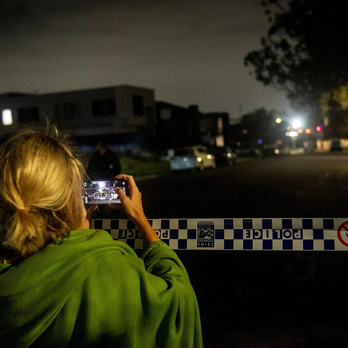 A woman records on her mobile phone as a police crime scene is established at the home of a suspect in Bonnyrigg, following a deadly shooting at Bondi Beach, on Dec 14.