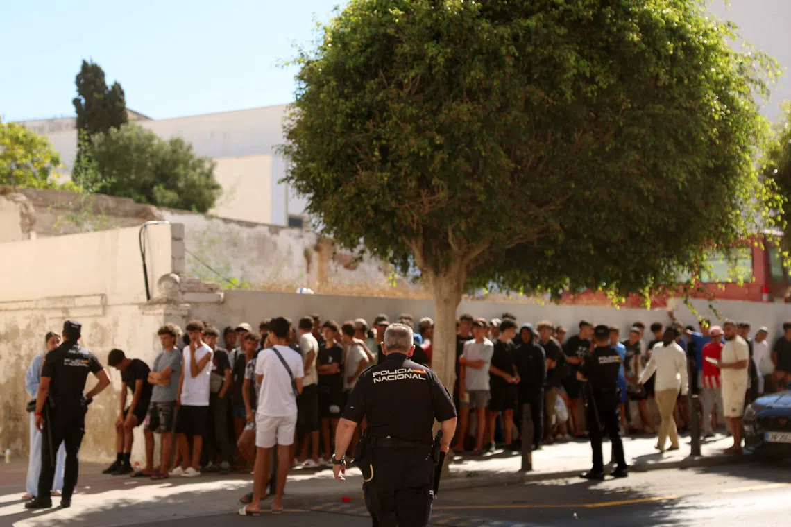 A group of people, some in uniform, gathered outdoors near a large tree.