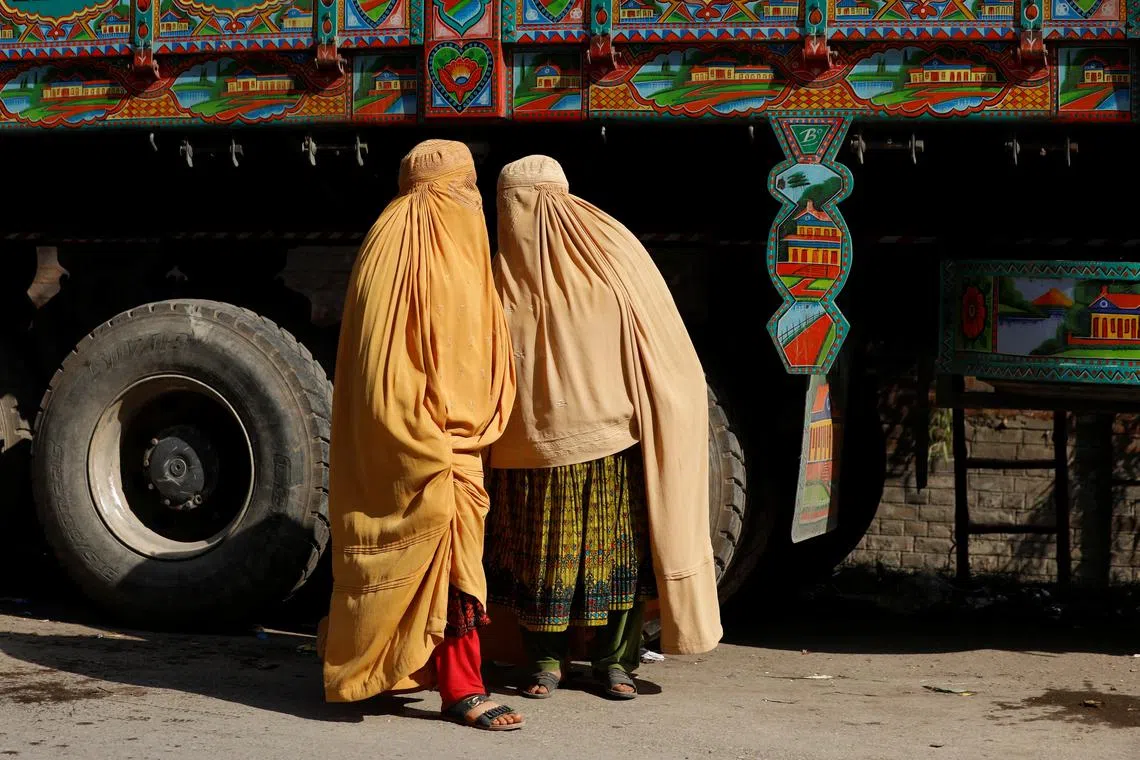 FILE PHOTO: Afghan women in burqa stand with a truck loaded with belongings as they return home, after Pakistan gives last warning to undocumented immigrants to leave, outside the United Nations High Commissioner for Refugees (UNHCR) repatriation centre in Azakhel town in Nowshera, Pakistan November 3, 2023. REUTERS/Fayaz Aziz/File Photo