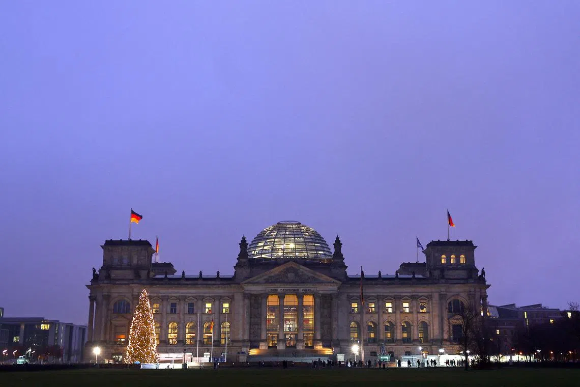 FILE PHOTO: German national flags fly atop the illuminated Reichstag building, the seat of Germany's lower house of parliament Bundestag, in Berlin, Germany December 9, 2022. REUTERS/Lisi Niesner/File Photo