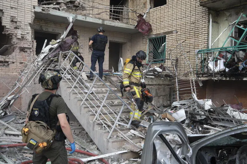 Emergency personnel are gathered outside a damaged brick building with a ladder leaning against it.