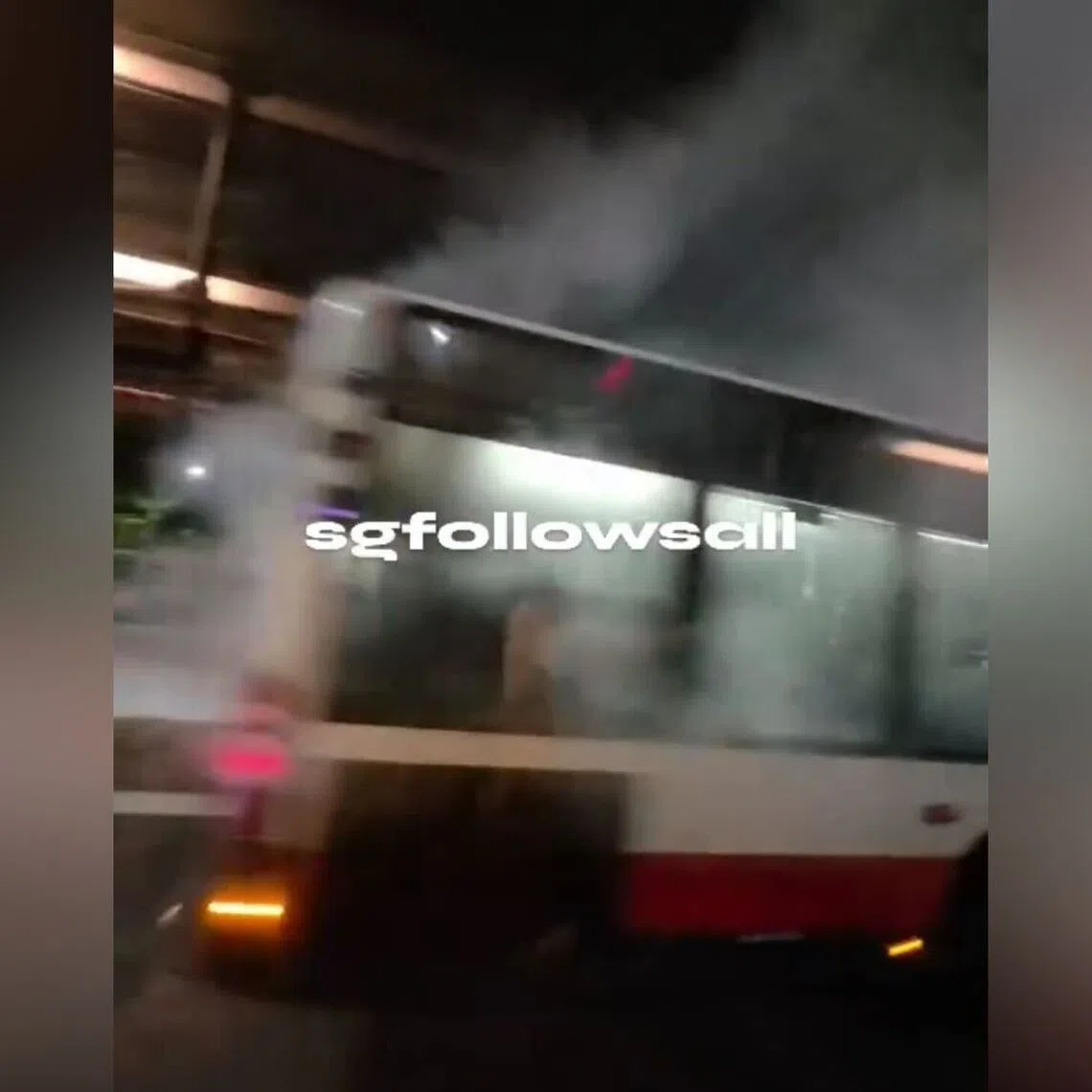 Smoke is seen rising from back half of the bus, which was stationary by the side of the road. 