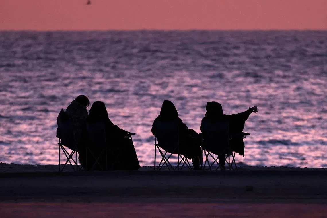 Women sit along the beach at sunrise, in Kuwait City on April 15, 2023. (Photo by YASSER AL-ZAYYAT / AFP)