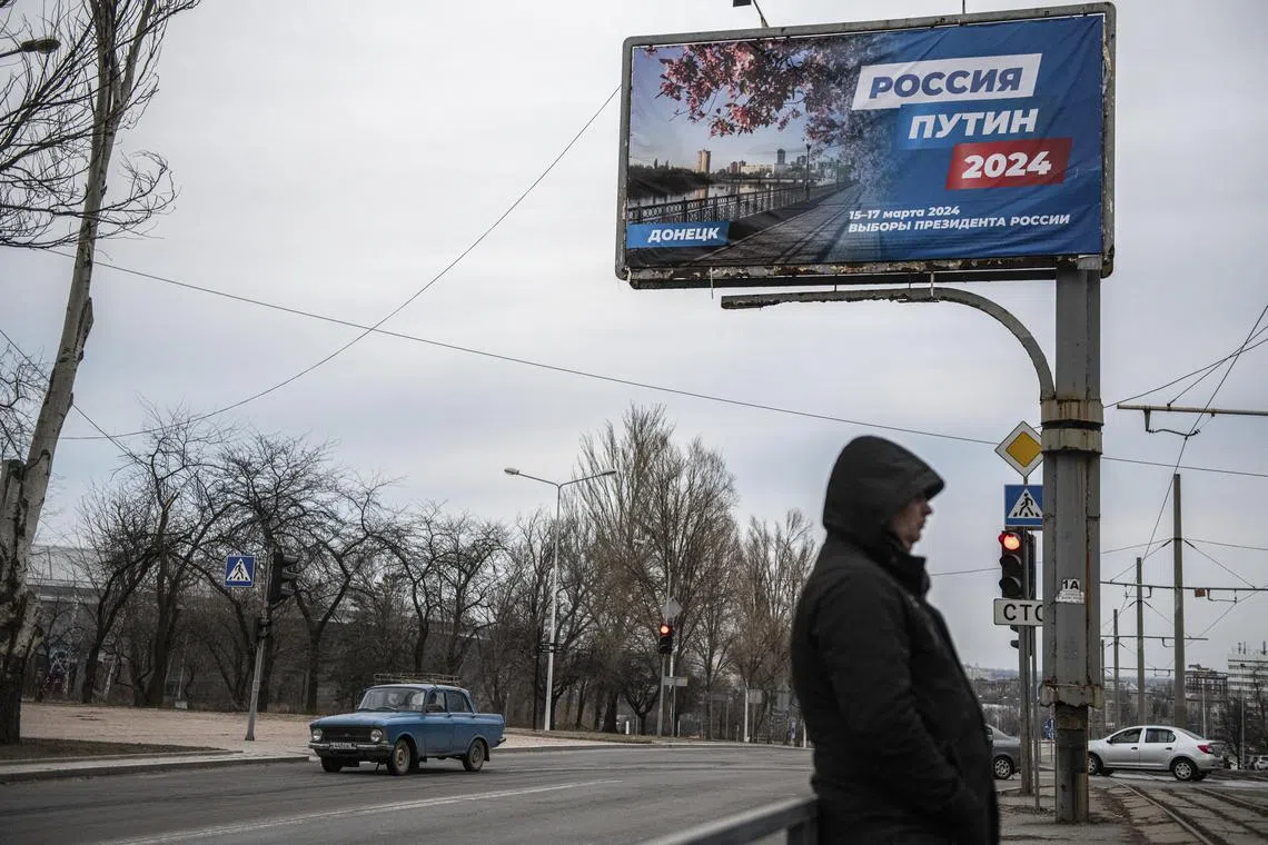 A man stands in front of a campaign poster for Russian president Vladimir Putin, reading "Russia, Putin, 2024", in downtown Donetsk, a Russian-occupied city in Ukraine.
