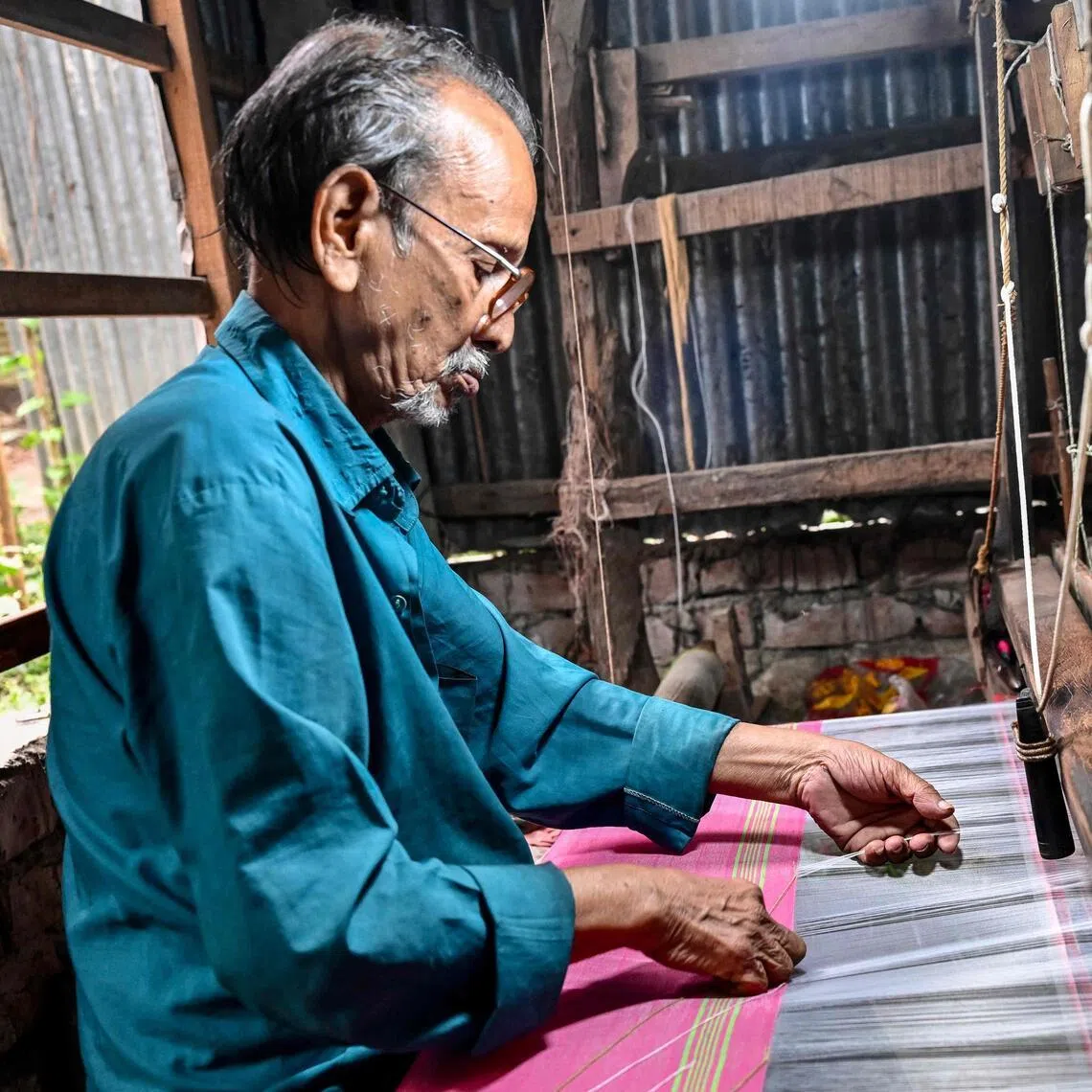 A Bangladeshi craftsman weaves fabric on a traditional handloom inside a workshop in Tangail on March 2, 2026. Bangladesh's Tangail sari is fighting for survival as weavers warn that automation and economic pressures are pushing the centuries-old craft to the brink despite its global acclaim. (Photo by Munir UZ ZAMAN / AFP) / To go with 'Bangladesh-Culture-Textile', FOCUS