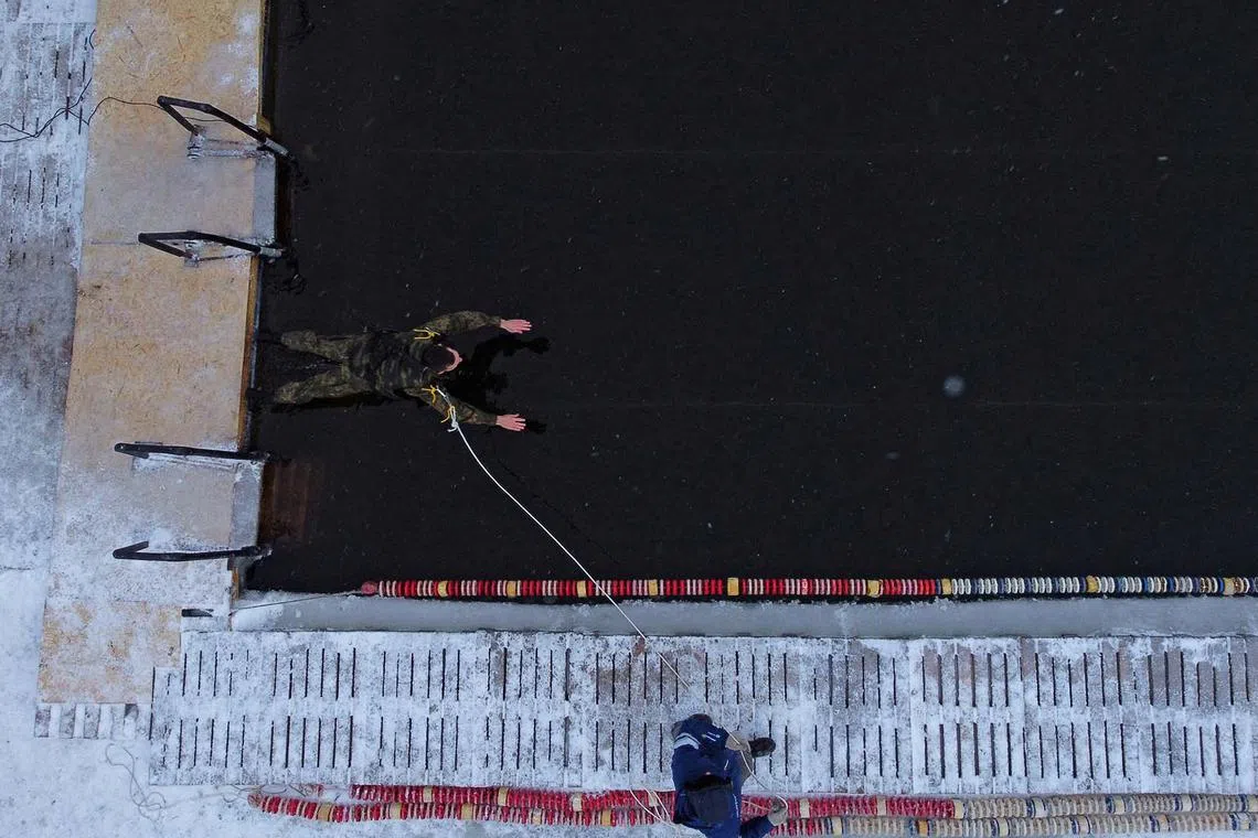 A cadet of the Tyumen Higher Military Engineer Command School wearing a bulletproof vest and carrying an assault rifle competes in a 25-metre race during a winter swimming tournament in Tyumen, Russia, Dec 11, 2022. 
