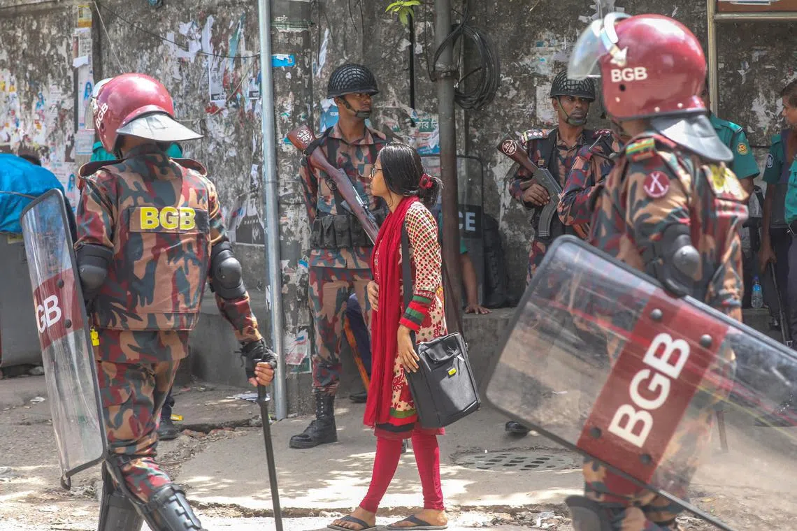 A woman walks along the Border Guard Bangladesh members patrolling on the street in Dhaka on July 26.
