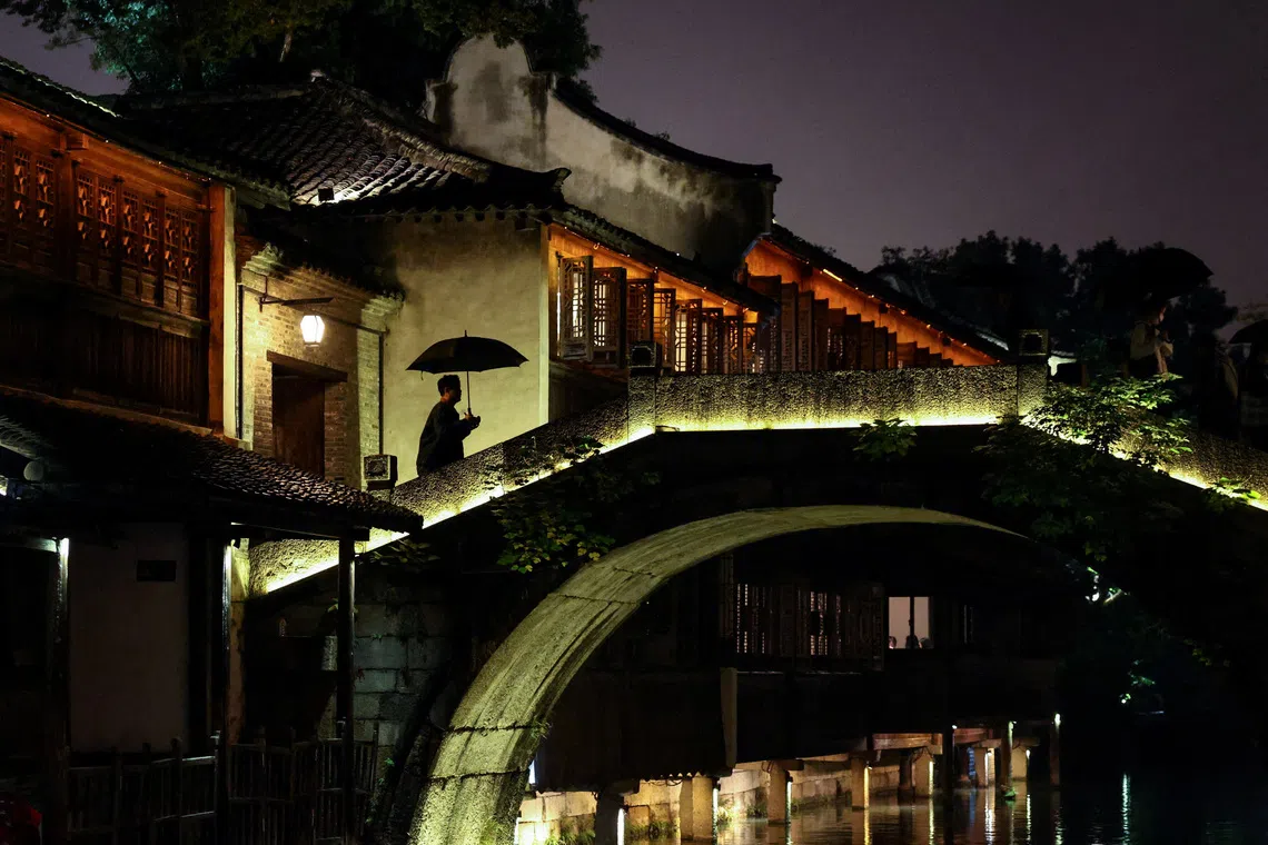 A person holding an umbrella walking past a bridge at Wuzhen town of Tongxiang city, Zhejiang province, China on Nov 6, 2025. 