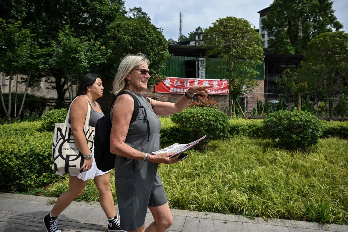 Ms Corinne Wilson (right) walking on a street as she holds flyers to look for her adopted daughter Loulee's (left) biological parents in Dianjiang county.