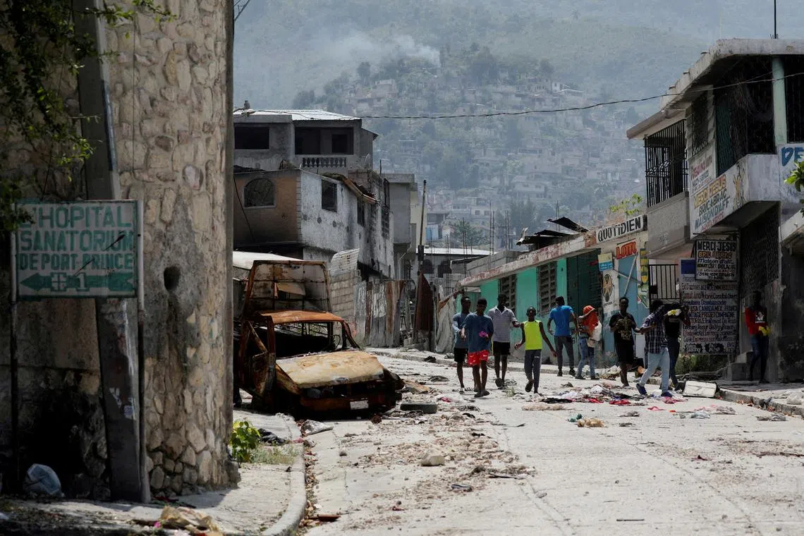 FILE PHOTO: People walk past a damaged car in the Carrefour Feuilles neighborhood, which was deserted due to gang violence, in Port-au-Prince, Haiti March 19, 2024. REUTERS/Ralph Tedy Erol/File Photo