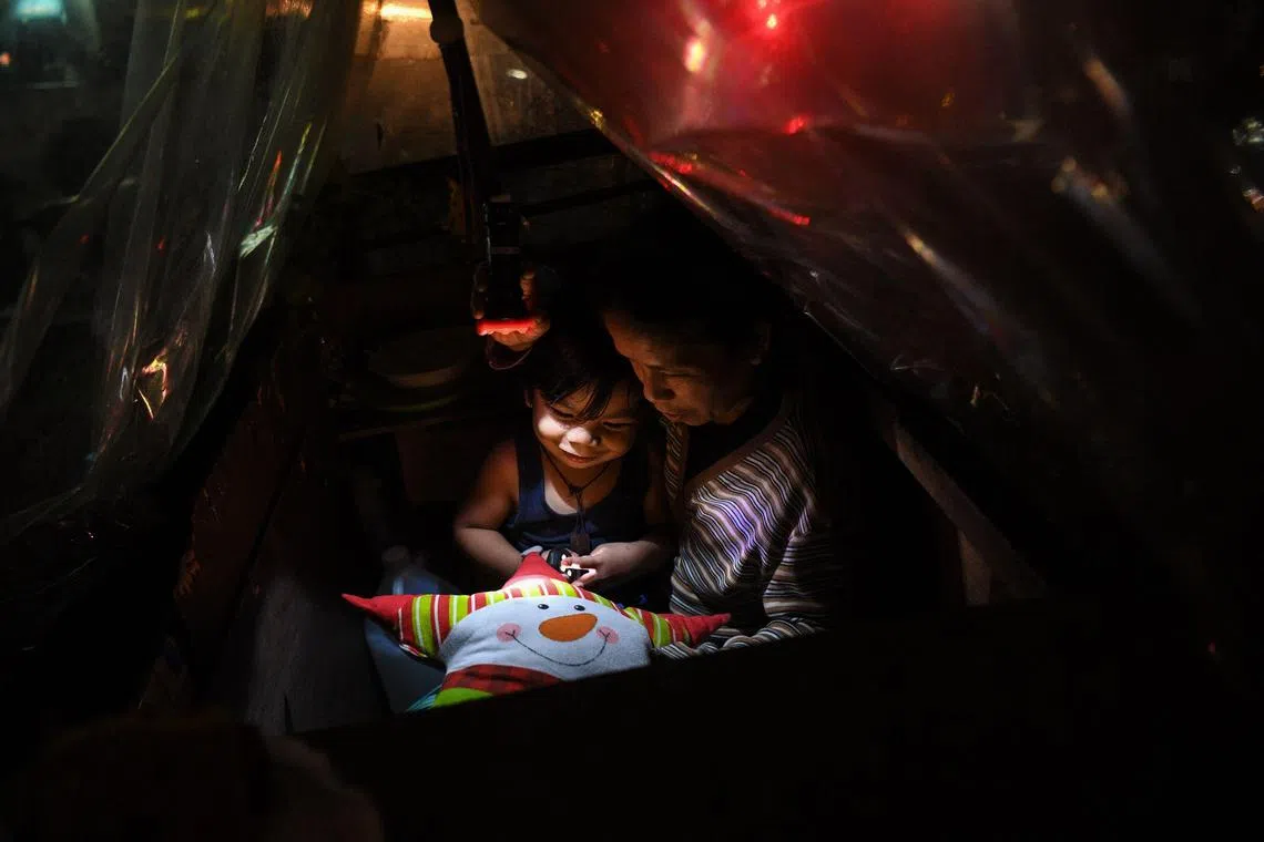 This photo taken on Nov 29, 2022 shows Ms Maricel Abawag and her son resting inside their pushcart 'home' next to a residential condominium building in Quezon City, suburban Manila.