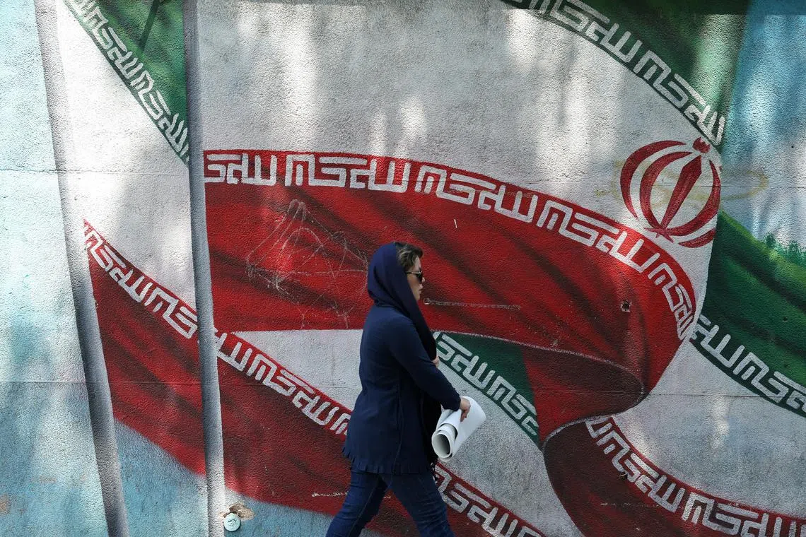 A woman walks next to a wall painting of Iran's flag in Tehran, as tensions remain high between Iran and Israel.
