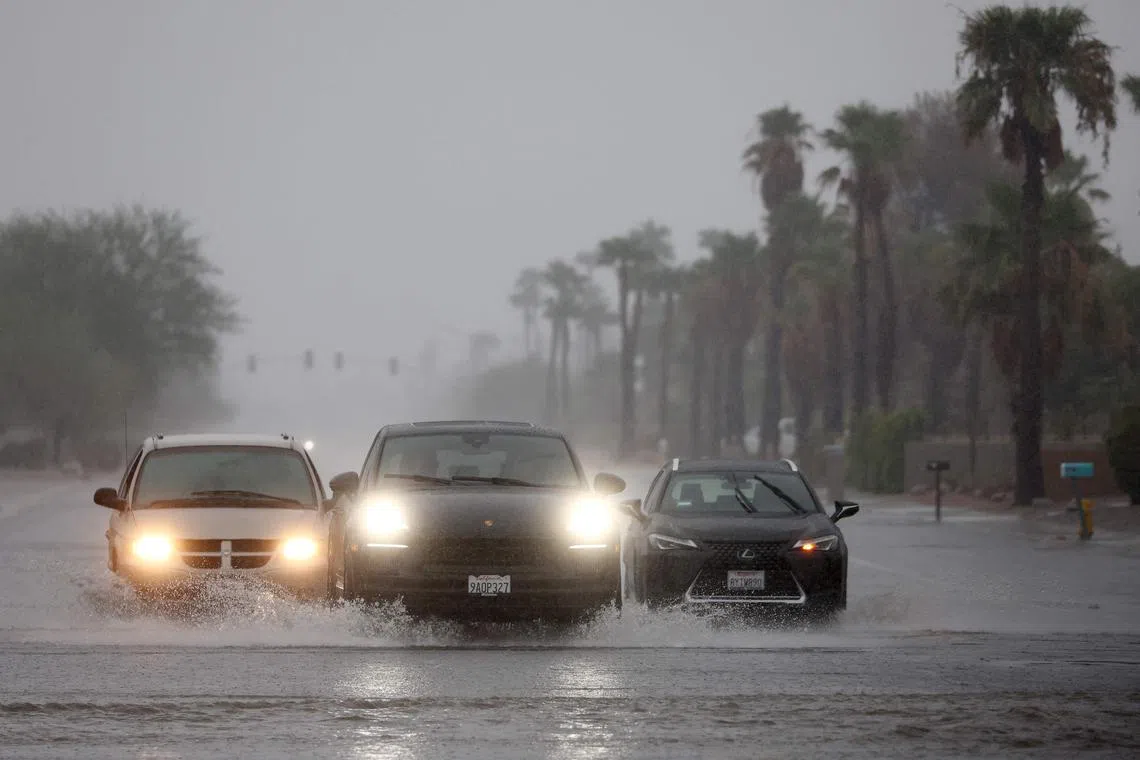 Vehicles drive along a flooded street as Tropical Storm Hilary approaches on Aug 20, 2023 in Palm Springs, California.