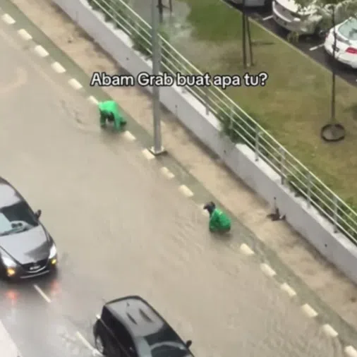 Two Grab riders were seen clearing clogged street drainage along a street in Kuala Lumpur.