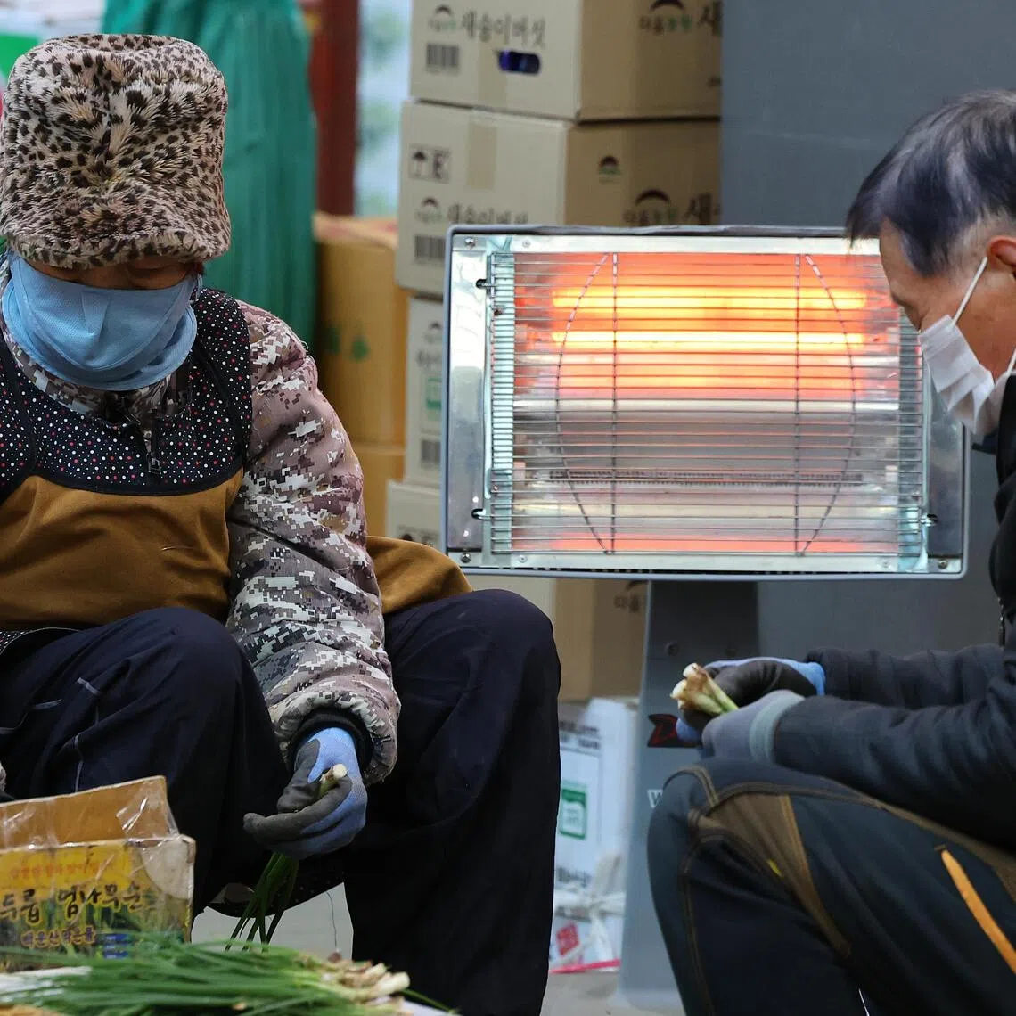 Shopkeepers trim scallions while warming themselves with an electric heater at a wholesale market in Incheon, South Korea.