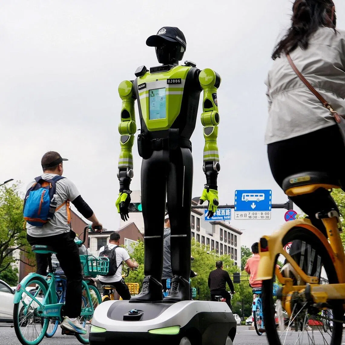 TOPSHOT - People cycle past a humanoid robot police officer in Hangzhou, in China’s eastern Zhejiang province on May 3, 2026 on the third day of a five-day national May Day holiday. The tech hub's traffic police deployed 15 humanoid robots in total to bolster their ranks on May 1. (Photo by Agatha CANTRILL / AFP)