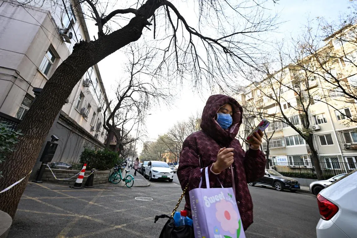 A woman wearing a face mask uses her phone while walking down a street in Beijing on Dec 5, 2023.
