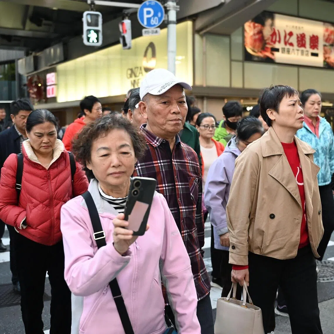 (FILES) Members of a Chinese tour group cross a road in the Ginza shopping district in Tokyo on November 17, 2025. The number of Chinese tourists in Japan plunged 45 percent in December from a year earlier, the transport ministry said on January 20, 2026, as a diplomatic row between Beijing and Tokyo rumbled on. (Photo by GREG BAKER / AFP)