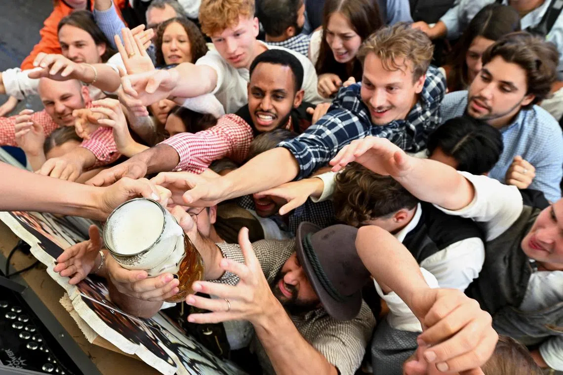 People reach out to catch the first mug of beer on the day of the official opening of the 189th Oktoberfest, the world's largest beer festival in Munich, Germany, September 21, 2024. REUTERS/Angelika Warmuth