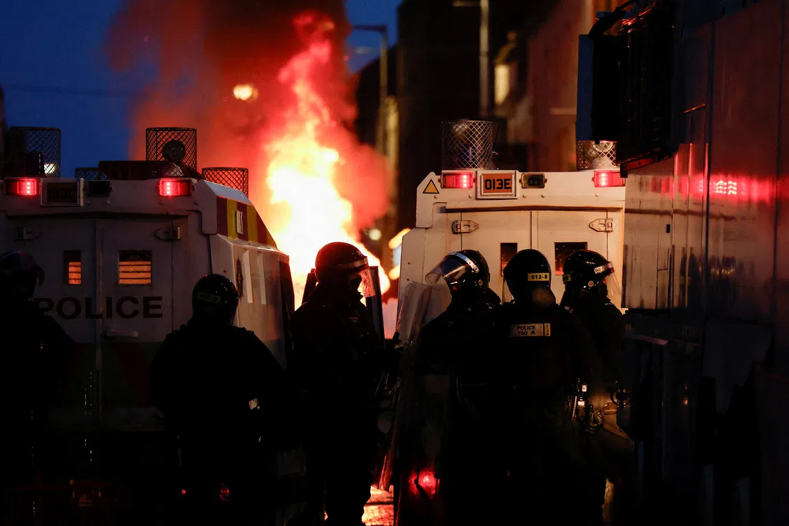 FILE PHOTO: Police officers stand guard behind police vehicles as flames rise during a the second night of riots, in Ballymena, Northern Ireland, June 10, 2025. REUTERS/Clodagh Kilcoyne/File Photo