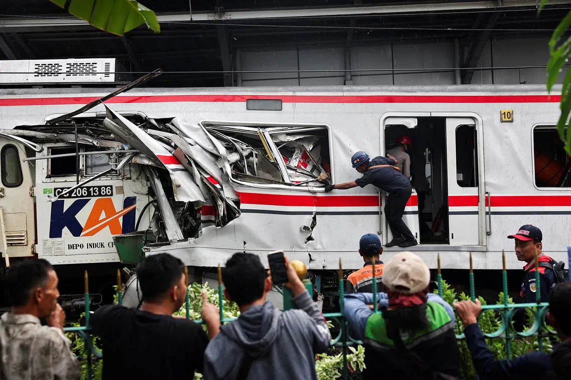 People watching a technician working at the site after a deadly collision between a commuter line train and a long-distance train.