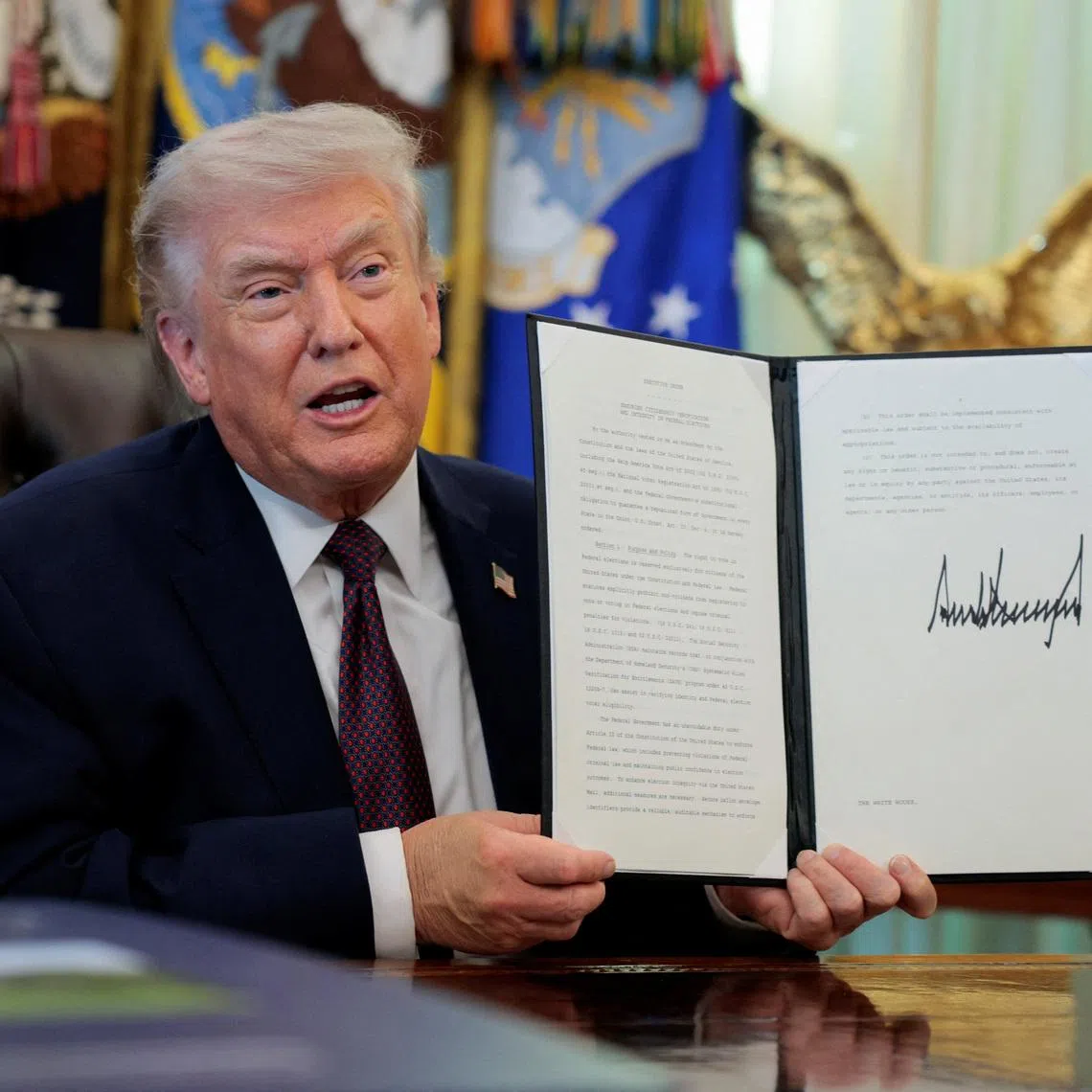 US President Donald Trump speaks as he shows a signed executive order on mail ballots, in the Oval Office of the White House.