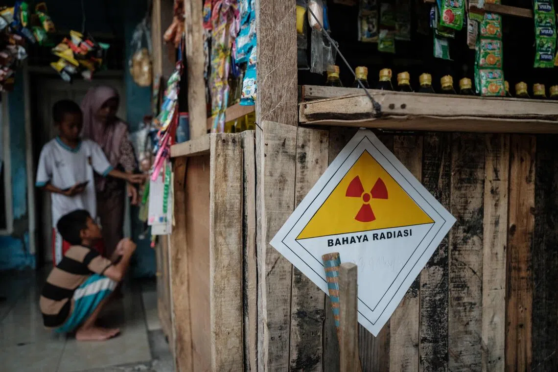 A warning sticker labelled “Danger Radiation” with a handwritten note showing “23.9 microsieverts per hour” is seen on the wall of a kiosk in front of a house next to the Modern Cikande Industrial Estate, where the radioactive isotope Caesium 137 was detected, in Sukatani, Banten province on October 13, 2025. An Indonesian task force found traces of radioactivity in 22 facilities at an industrial zone near the capital, weeks after US authorities recalled potentially contaminated frozen shrimp. (Photo by Yasuyoshi CHIBA / AFP)