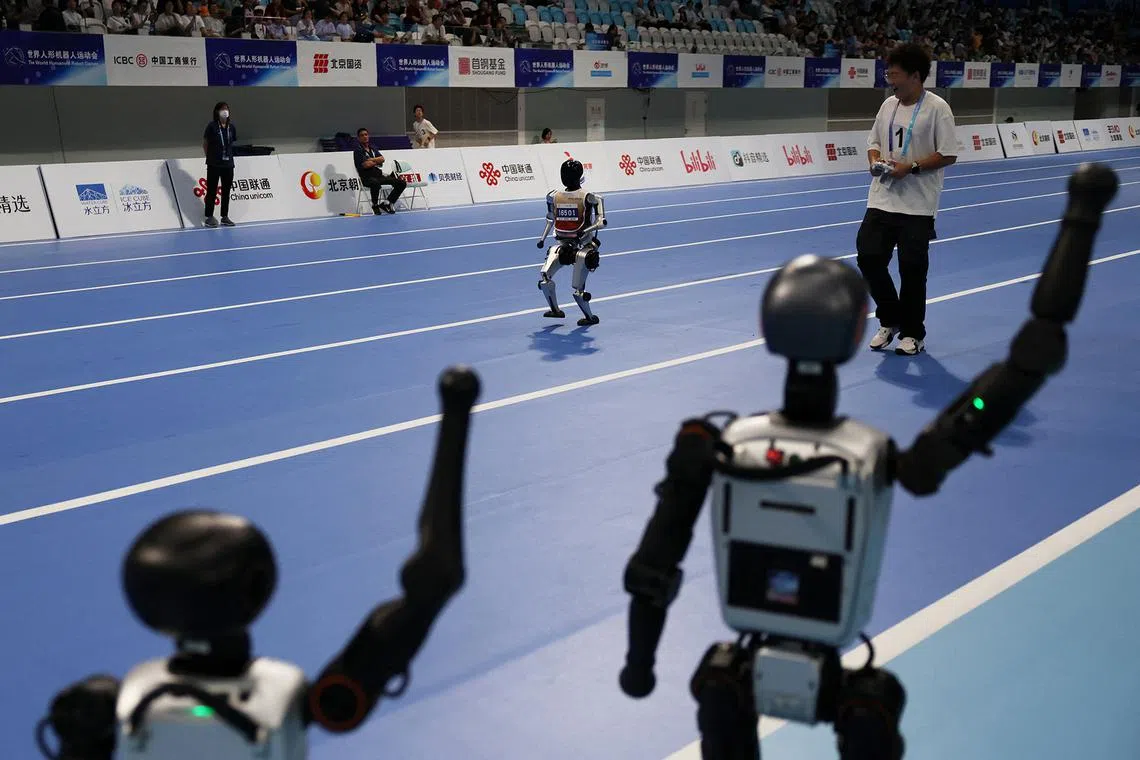 Booster Robotics humanoid robots cheering as a humanoid robot takes part in a 400m race at the inaugural World Humanoid Robot Games, at the National Speed Skating Oval in Beijing, China, on Aug 15, 2025. 