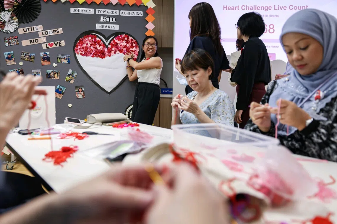 Ms Ong Poh Suan, 49, lead of Khoo Teck Puat Hospital (KTPH) and Yishun Community Hospital (YCH) Arts Interest Group, pinning hearts on a mobile board at Yishun Community Hospital. This activity is part of the 1510 Crochet Heart Challenge, where 50 staff members aim to crochet 1,510 hearts celebrating KTPH's 15th and YCH's 10th anniversaries. Each heart represents a $2 donation, with all contributions going to the National Kidney Foundation, and funded by staff themselves. The challenge runs from 18 September to 1 October, with the completed heart artwork to be unveiled during Patient Service Associate (PSA) Day on 15 October.