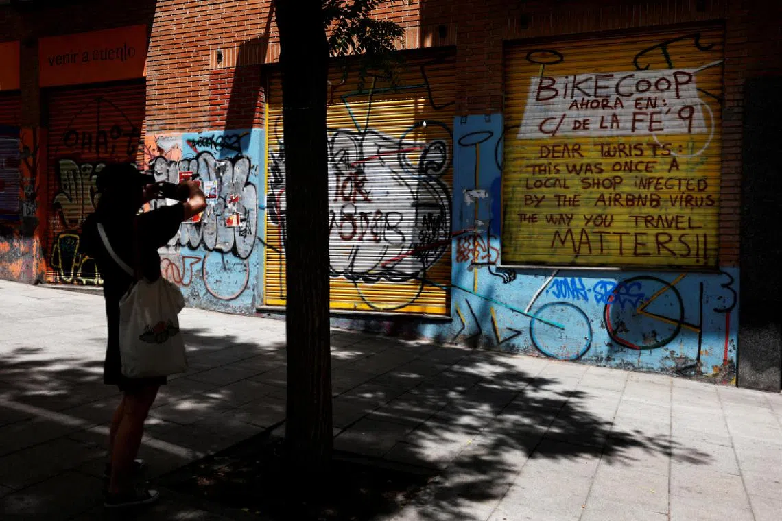 A woman in Madrid takes a photo of a message aimed at tourists and against Airbnb vacation rentals, on the outside of what used to be a local store.