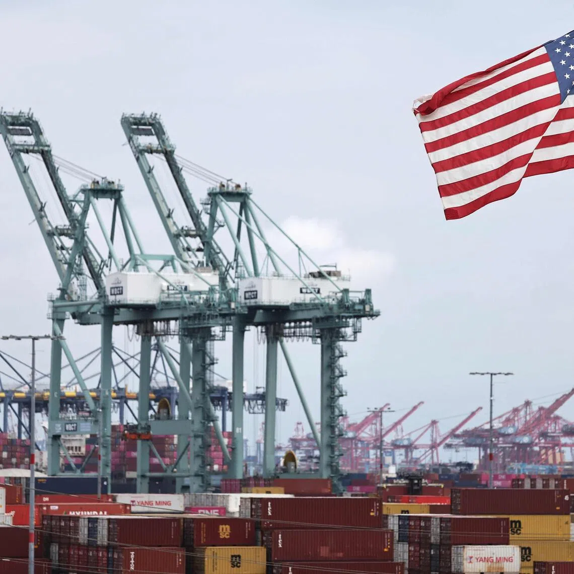 LOS ANGELES, CALIFORNIA - SEPTEMBER 26: An American flag flies in front of shipping containers and cranes at the Port of Los Angeles on September 26, 2025 in Los Angeles, California. President Trump yesterday announced a slew of new tariffs on pharmaceutical products, heavy trucks, kitchen cabinets and upholstered furniture which go into effect on October 1.   Mario Tama/Getty Images/AFP (Photo by MARIO TAMA / GETTY IMAGES NORTH AMERICA / Getty Images via AFP)