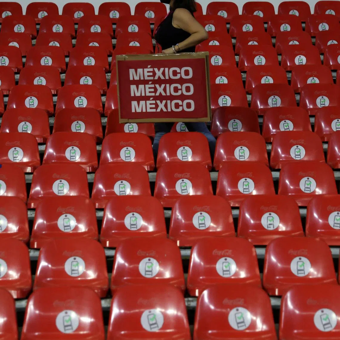FILE PHOTO: A woman carries a promotional item through empty stands at a World Cup qualifying match between Mexico and Panama after the Mexican Football Federation adopted a \"zero tolerance\" policy against homophobic chants and suspended ticket sales to fans, in Estadio Azteca stadium in Mexico City, Mexico February 2, 2022. REUTERS/Edgard Garrido/File Photo