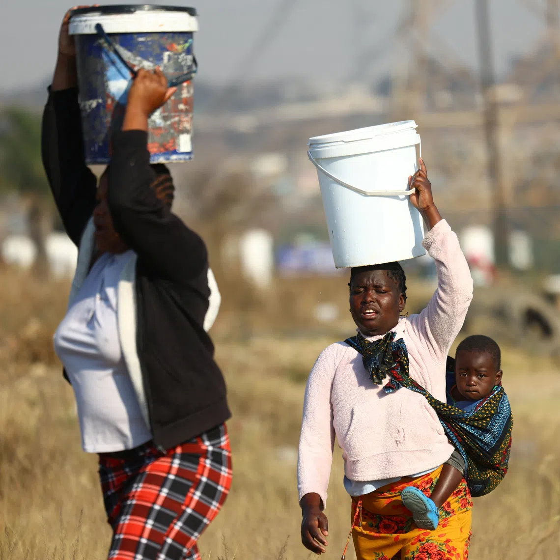 Residents carrying buckets filled with water collected from a nearby filling station in Olievenhoutbosch, north of Johannesburg, on Aug 7.
