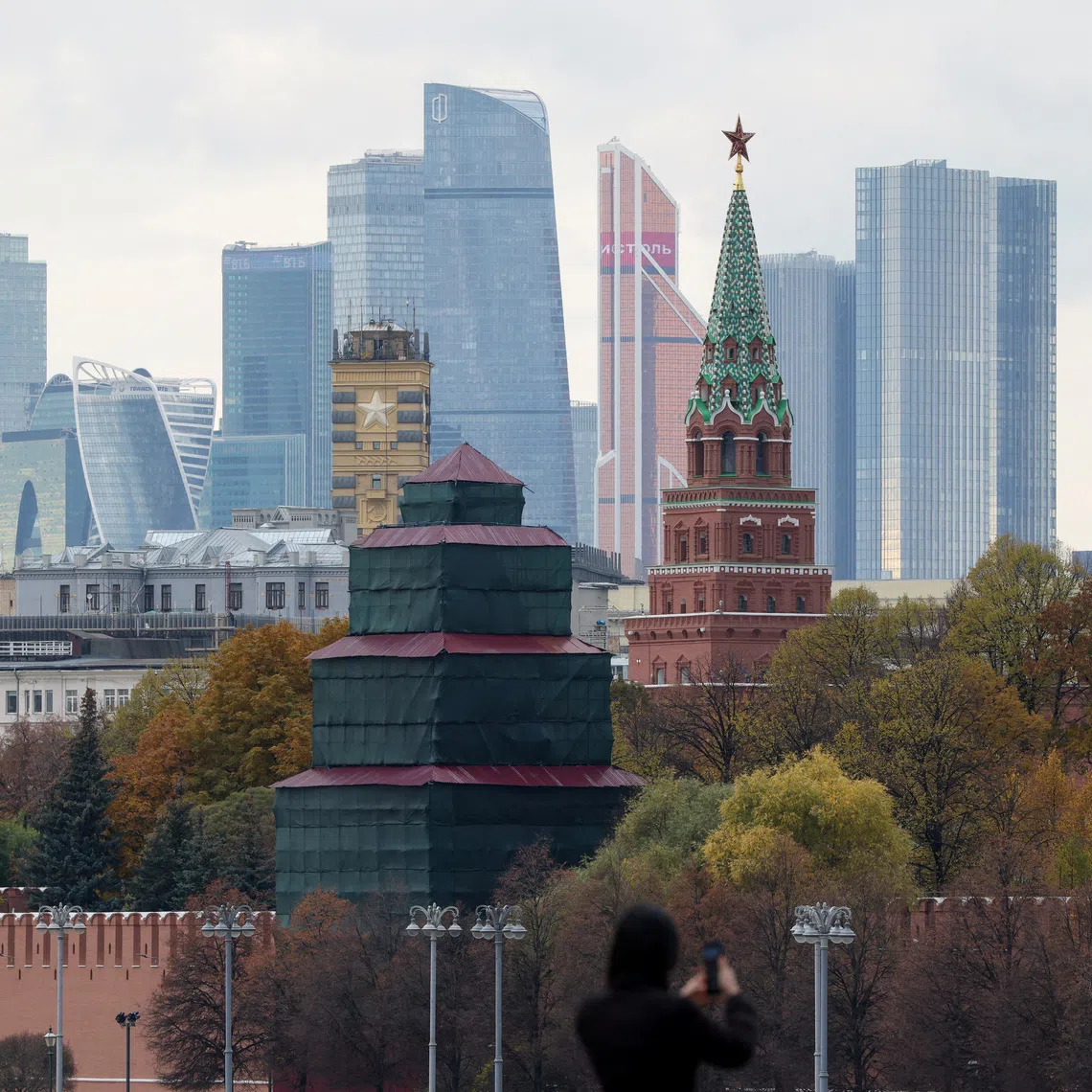 FILE PHOTO: A pedestrian uses a mobile phone while standing on a bridge near the Kremlin wall, with the skyscrapers of the Moscow International Business Centre, also known as Moskva-City, visible in the distance in Moscow, Russia, October 23, 2025. REUTERS/Ramil Sitdikov/File Photo
