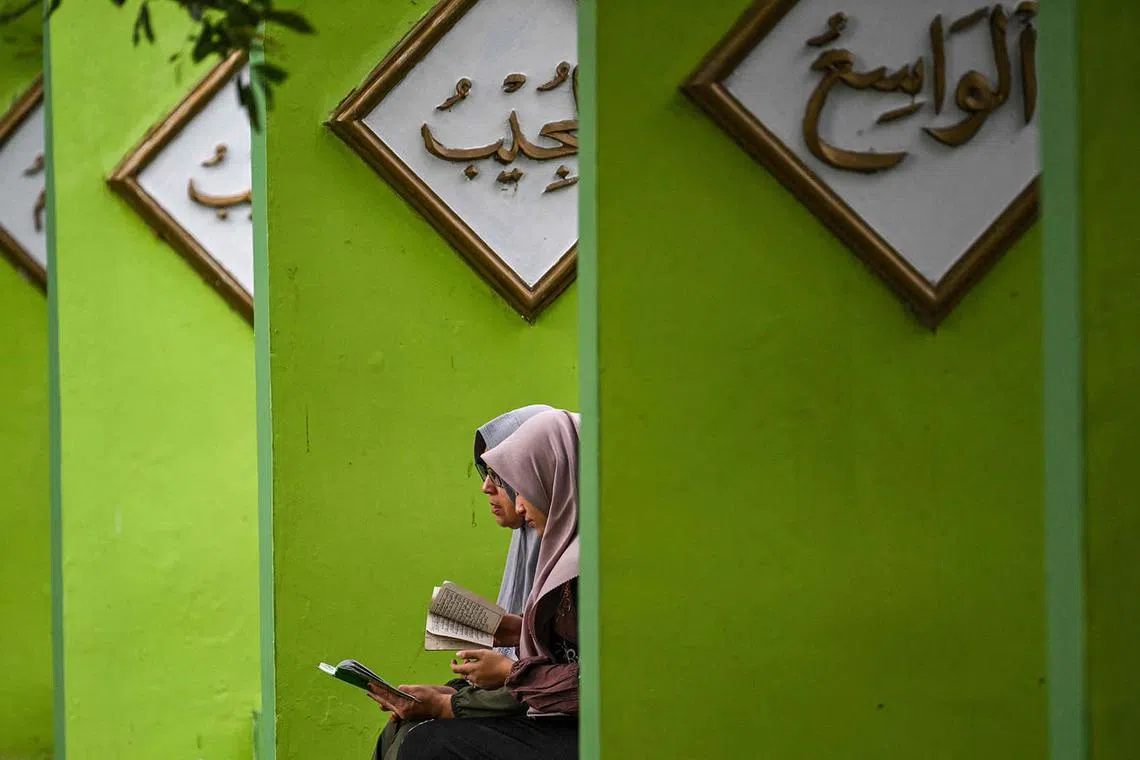 Two women reciting the Quran as they visit a mass burial cemetery to commemorate the 19th anniversary of the 2004 Indian Ocean earthquake and tsunami which killed over 200,000 people in 14 countries with Aceh recording the highest death toll, in Banda Aceh on Dec 26, 2023. 