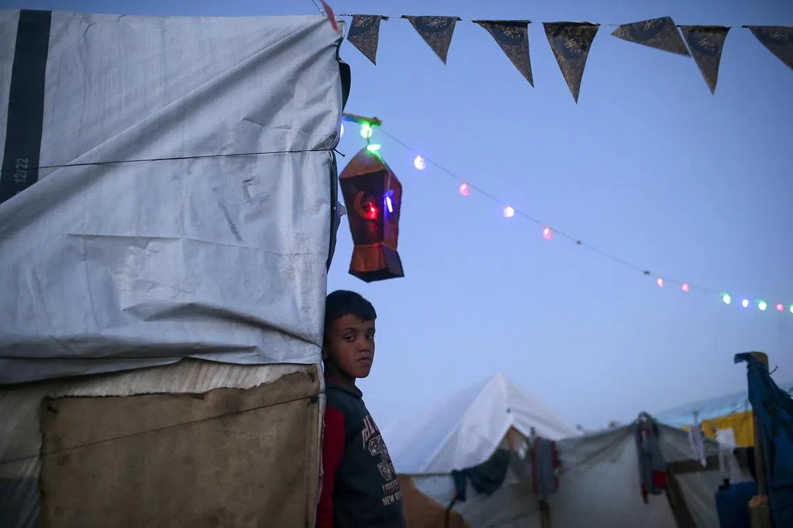 A displaced Palestinian child stands outside his family’s tent, decorated with lanterns to mark the holy month of Ramadan.