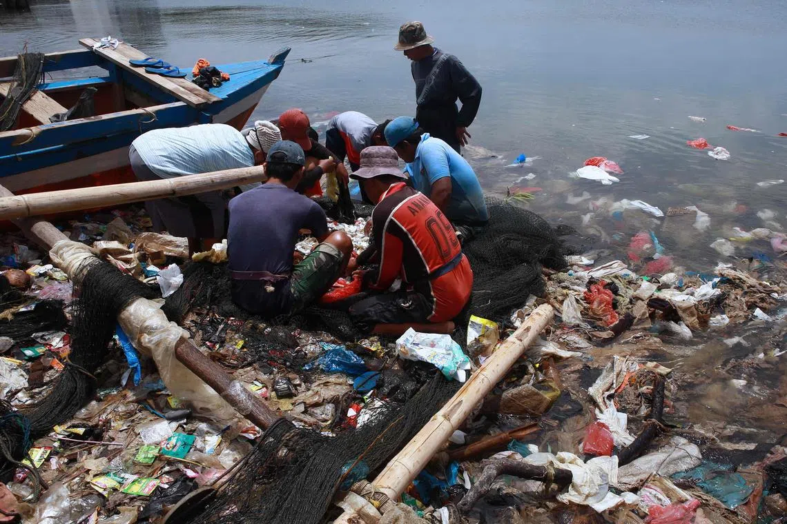 Fishermen sort their catch from a net as they fish in polluted waters filled with plastic waste in Bandar Lampung on February 21, 2022. (Photo by PERDIANSYAH / AFP)
