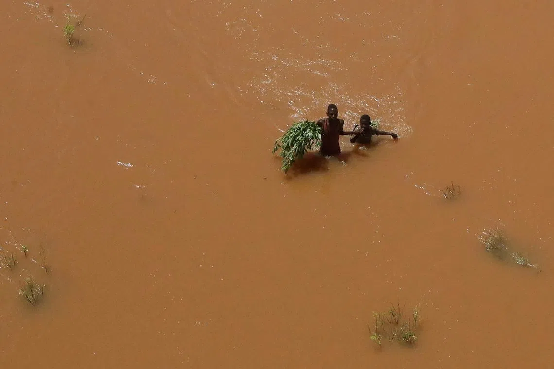 People holding on to plants as they wade through flood waters after they were displaced following heavy rains in Garsen, Tana Delta within Tana River county, Kenya Nov 23, 2023. 