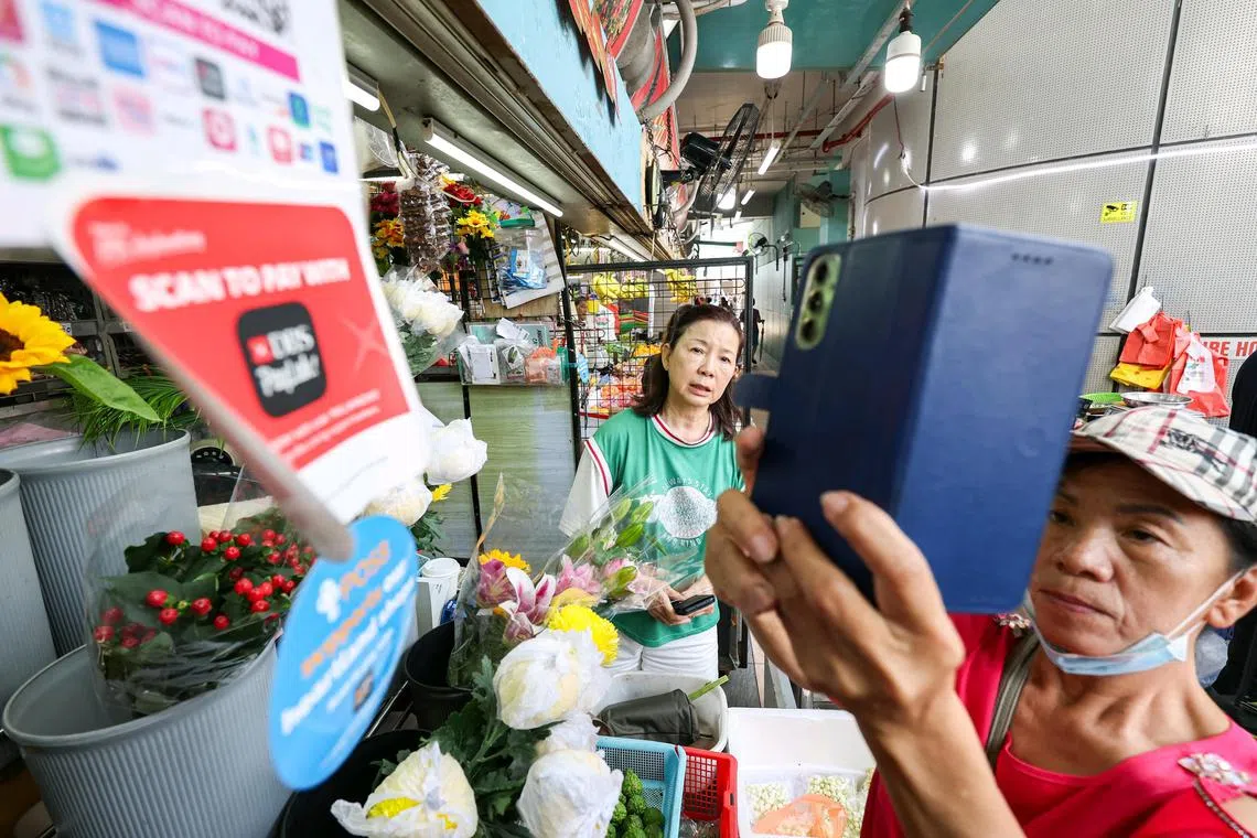 ST20241013_202483900956/gcdbs13/Brian Teo/Gabrielle Chan EH/(From Left) 
Madam Zhen Yue Hui, 63, Retiree, scanning the DBS QR payment as Madam Ivy Tan, 63, Jasmine Florist owner, prepares the flowers that Madam Zhen bought from her stall at Toa Payoh West Market and Food Centre on Oct 13, 2024. Since POSB offered over two million cash back rewards and discounts to heartland merchants as part of their Support Our Heartlands campaign in August, there has been a 40 percent boost in sales for hawkers and wet market stall holders. ST PHOTO: BRIAN TEO.