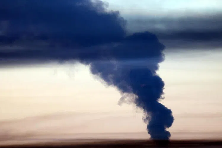 A column of dark smoke rising into the sky from a distant fire.