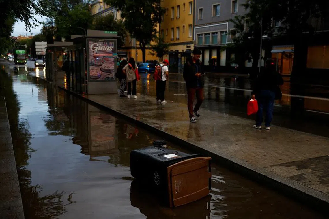 People wait for the bus by a flooded road caused by heavy rain, following a red alert for a severe storm from Spain's State Meteorological Agency (AEMET), in Madrid, Spain, September 4, 2023. REUTERS/Susana Vera