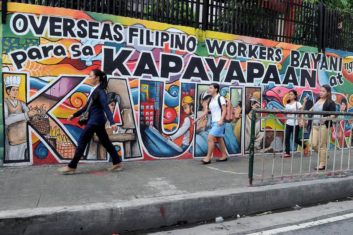 People walk past a mural honouring overseas Filipino workers in Manila on July 7, 2014. The government estimates there are ten million overseas Filipino workers, or about a 10th of the population, whose dollar remittances account for about 10 percent of gross domestic product. AFP PHOTO / Jay DIRECTO (Photo by JAY DIRECTO / AFP)