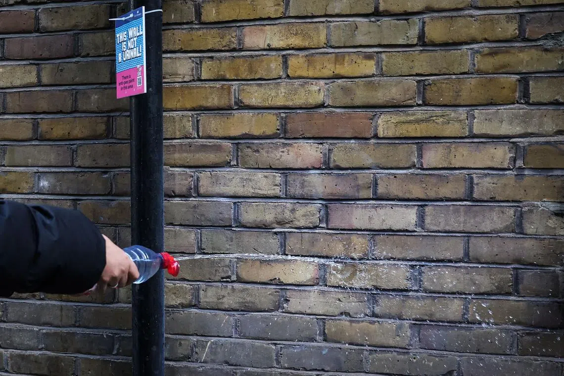 Local councillor Aicha Less spraying water, which bounces back, on a wall treated with an anti-pee paint in London's Soho district.