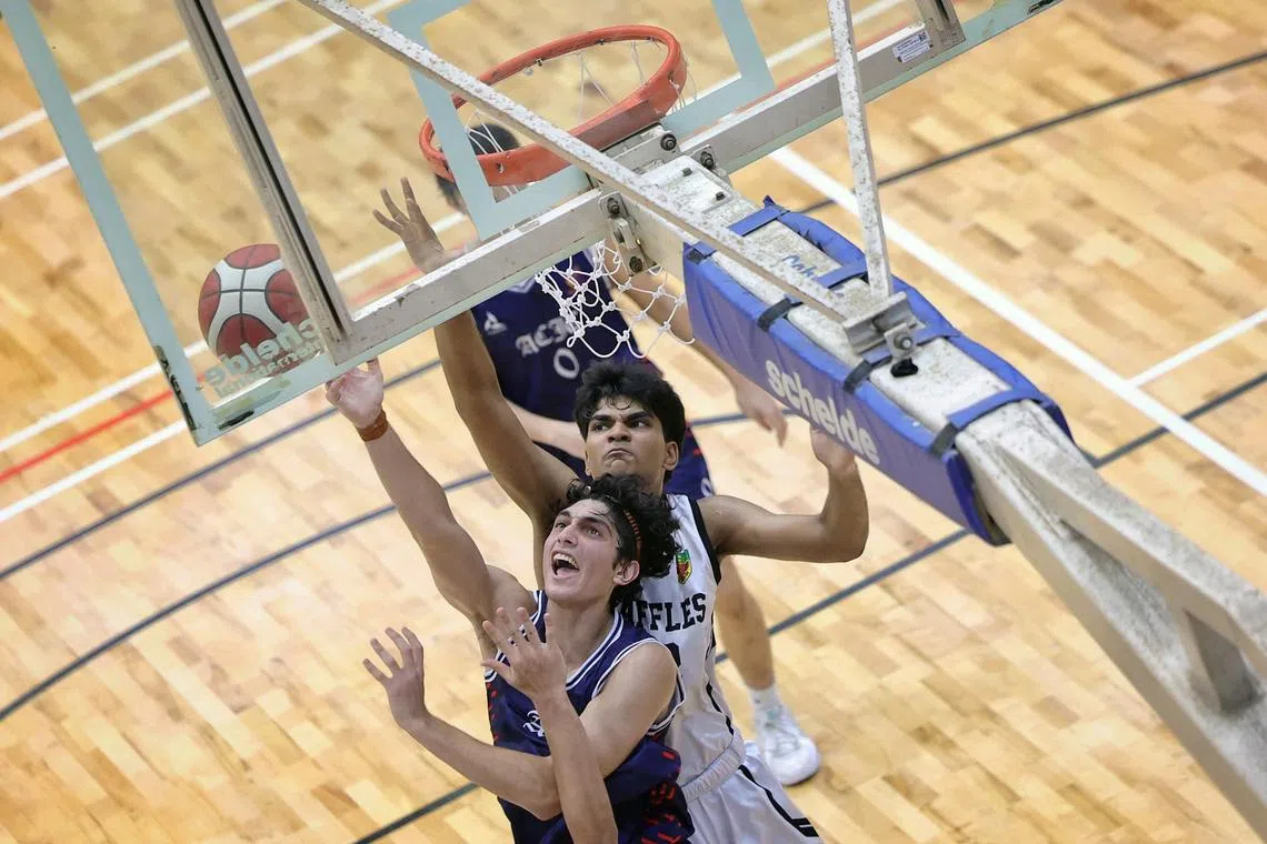 A Adityah da Raffles Institution (em branco), tentando bloquear um layup reverso do capitão Eshan Kaul, capitão Kaul (em azul escuro) nos Jogos Nacionais da Escola, uma final de basquete para meninos da Div no Jurong East Sports Hall em 23 de maio de 2025.